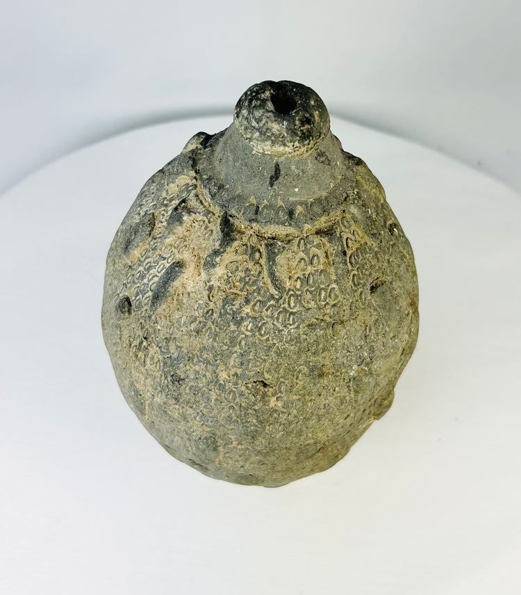 Islamic ceramic hand grenade from Greater Persia, 10th–12th century CE, shown in a top-angled view highlighting its engraved neck, rounded body, and aged patina on a white background.
