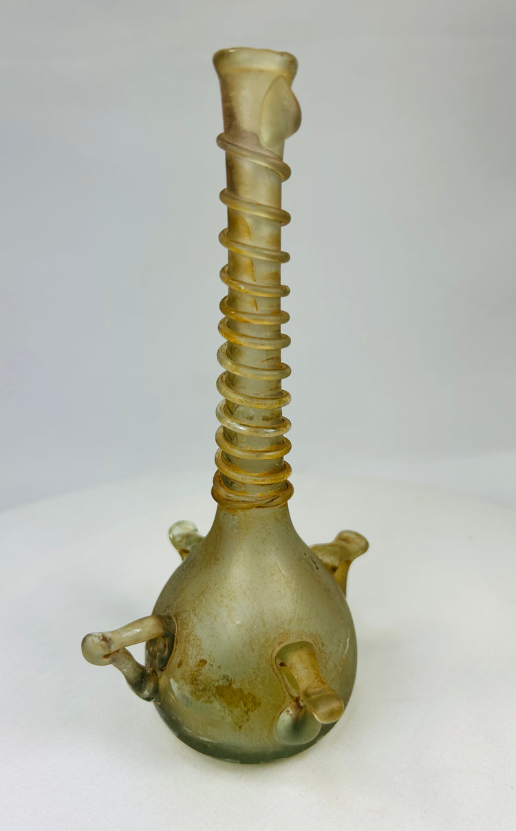 Angled right view of early Islamic glass bottle with long ribbed neck and twin loop handles, pale green tone.