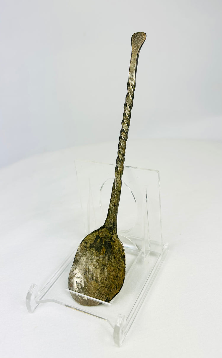 Slight left view of ancient bronze spoon with twisted stem and encrusted green patina.
