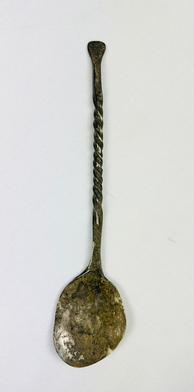 Top-down view of ancient bronze spoon with narrow handle and circular bowl, aged bronze patina.