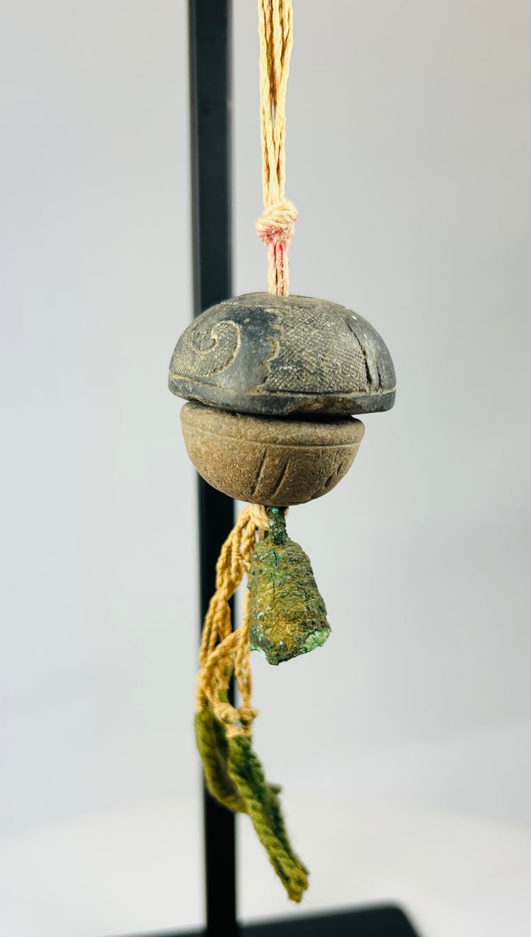 Angled view of ancient bronze bell pendant highlighting verdigris surface and hanging cord texture