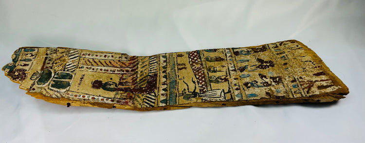 Angled perspective of ancient Egyptian coffin panel displaying faded polychrome hieroglyphs and symbolic motifs