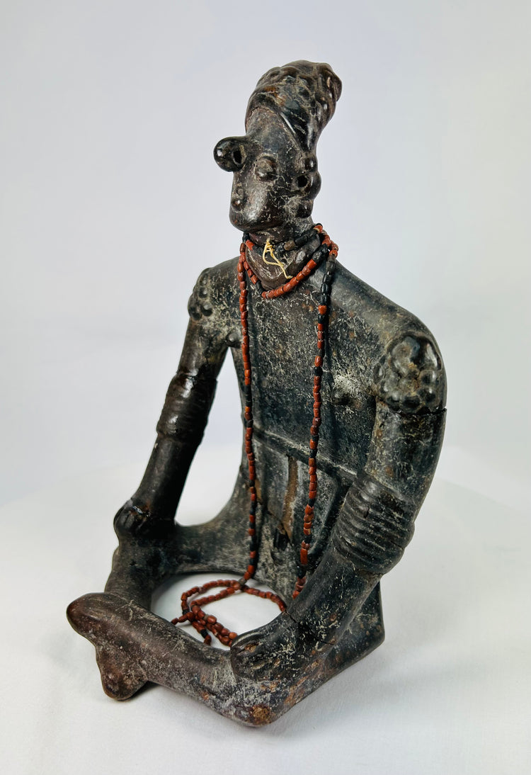 Three-quarter angled view highlighting serene expression, red beads, and cross-legged seated pose.