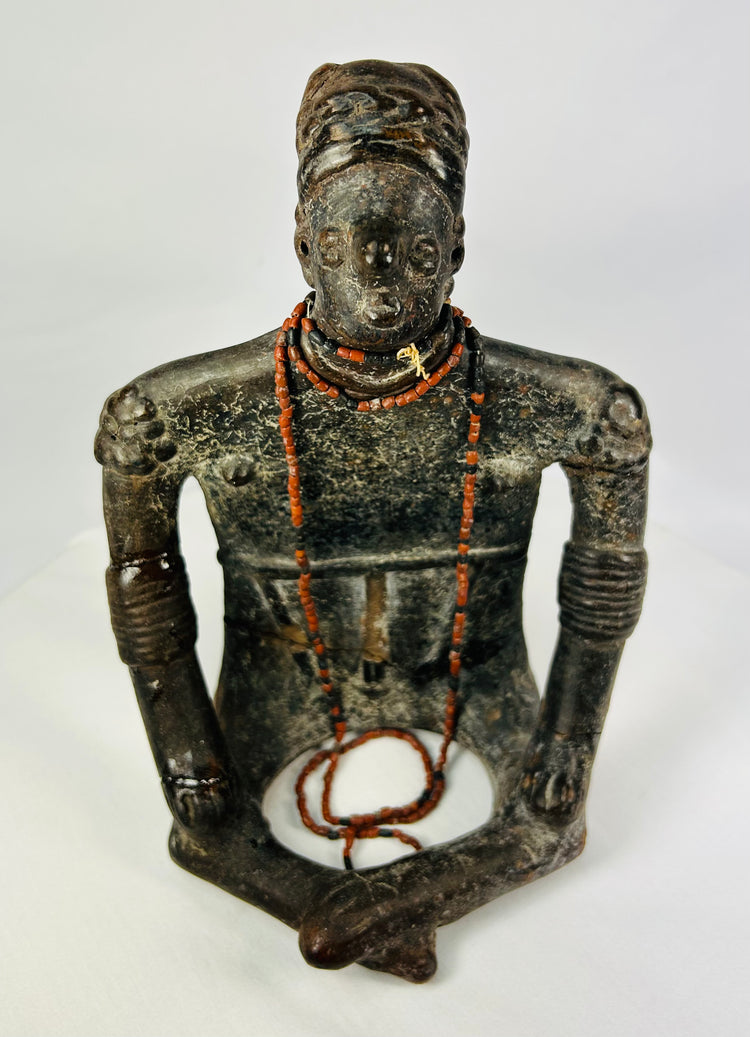 Close-up frontal image showing intricate facial modeling, bead adornments, and ritual posture.
