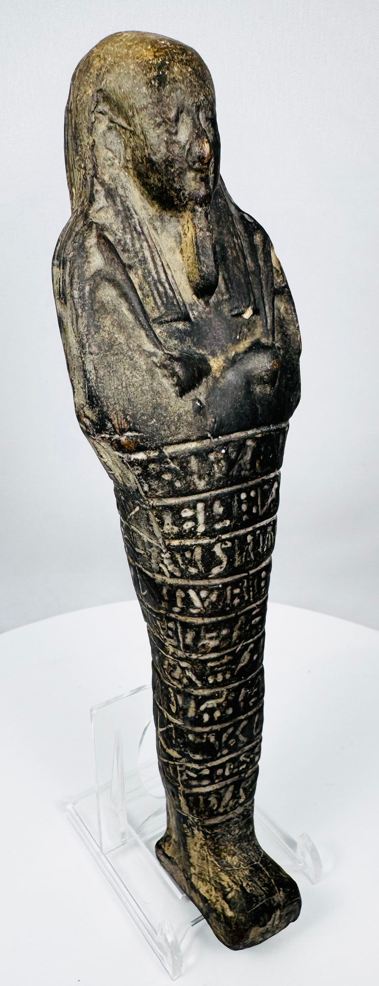 Three-quarter view of a Kushite-Saite period Egyptian shabti with striated wig and hieroglyphic inscription