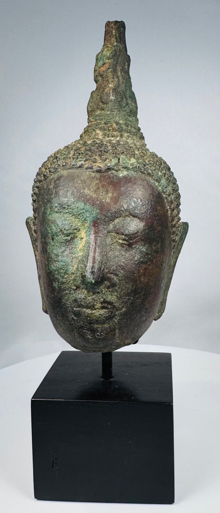 Bronze Buddha head with tightly modeled curls and elongated facial features