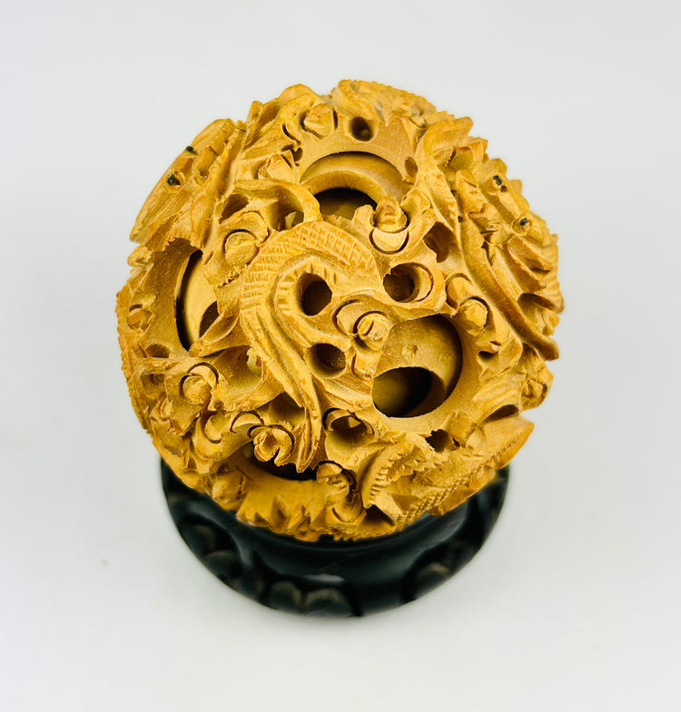 Chinese carved puzzle ball showing dragon relief work and inner rotating spheres on a black stand against a white background.