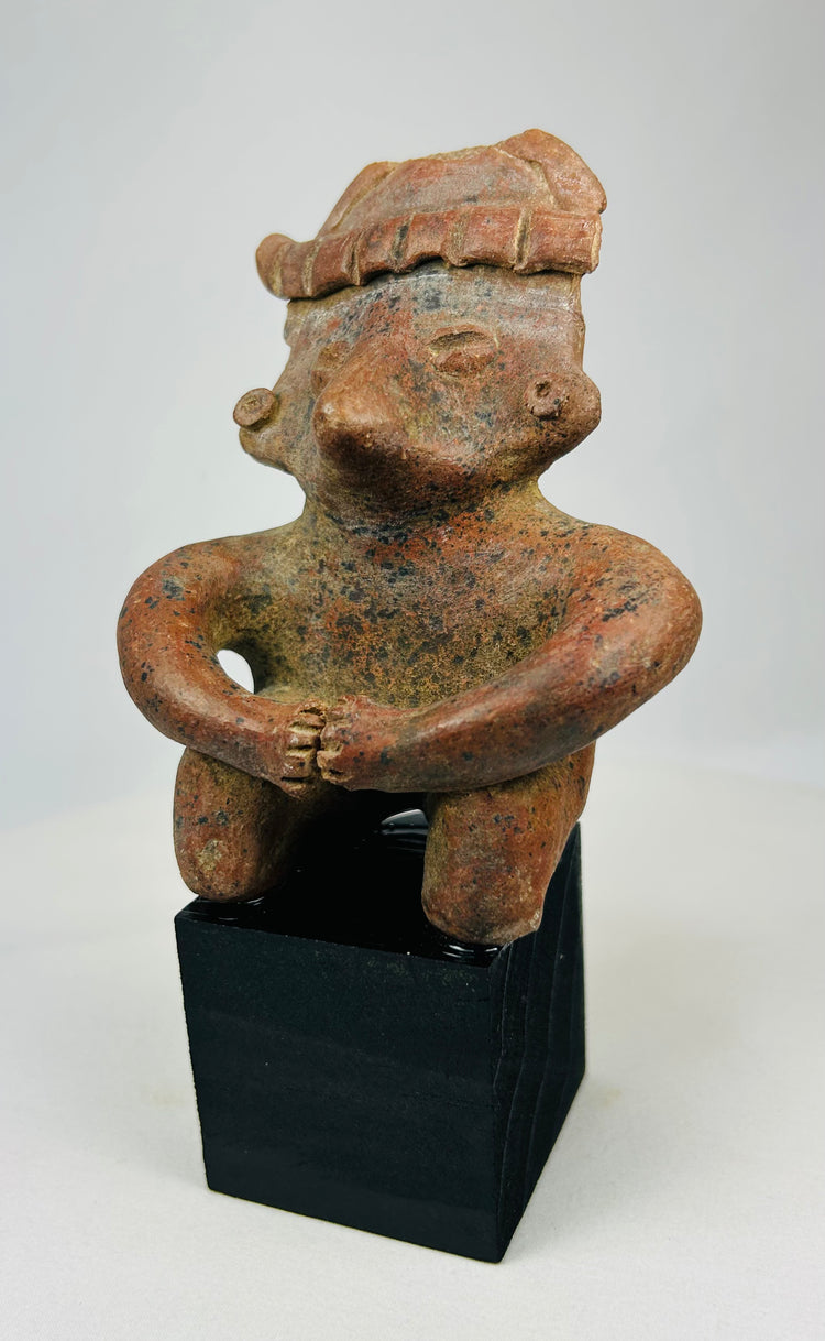 Ancient Nayarit figurine with rounded body and headdress on museum display stand.