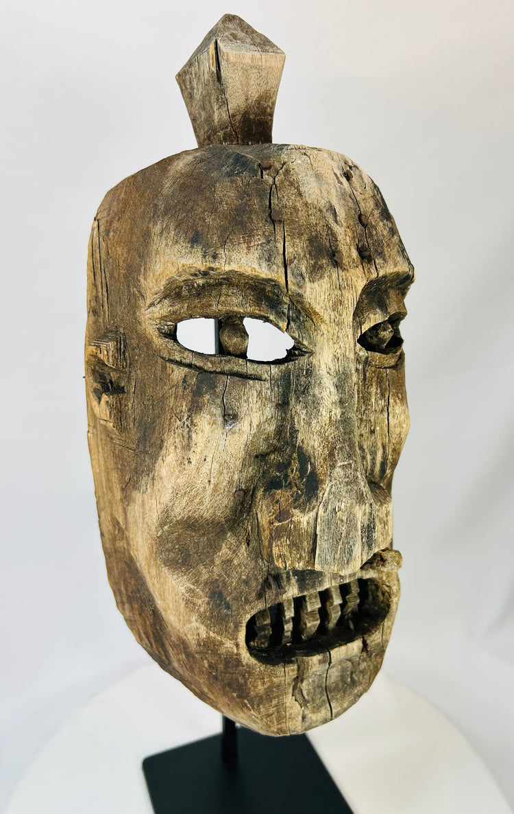 Side profile of a carved wooden ritual mask showing deep patina and sculpted facial contours.