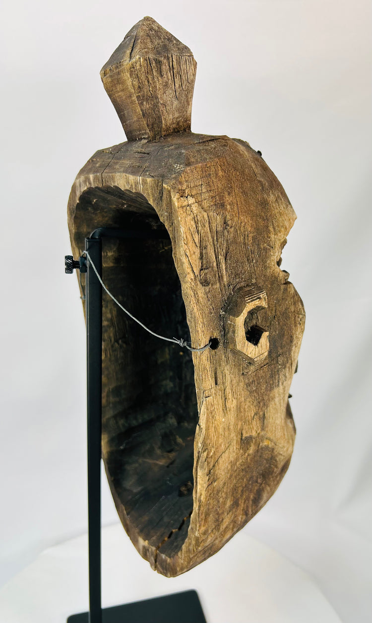 Left-side perspective of an old wooden ceremonial mask mounted on a display stand.