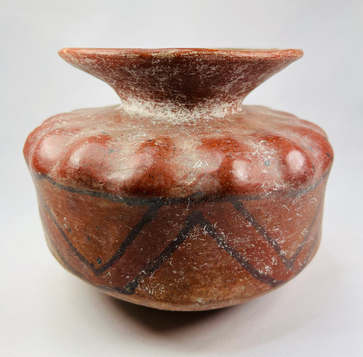 Side view of a Pre-Columbian terracotta vessel with zig-zag geometric paint and scalloped shoulder.