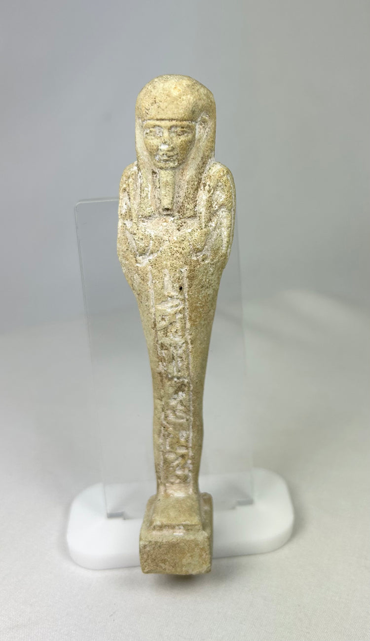Ancient limestone ushabti on a clear acrylic stand with visible mineral deposits