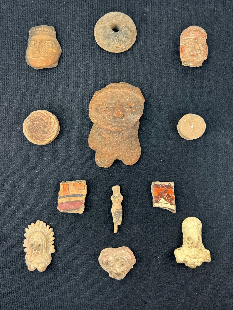 Pre-Columbian terracotta faces, idols, and pottery pieces arranged in a display frame