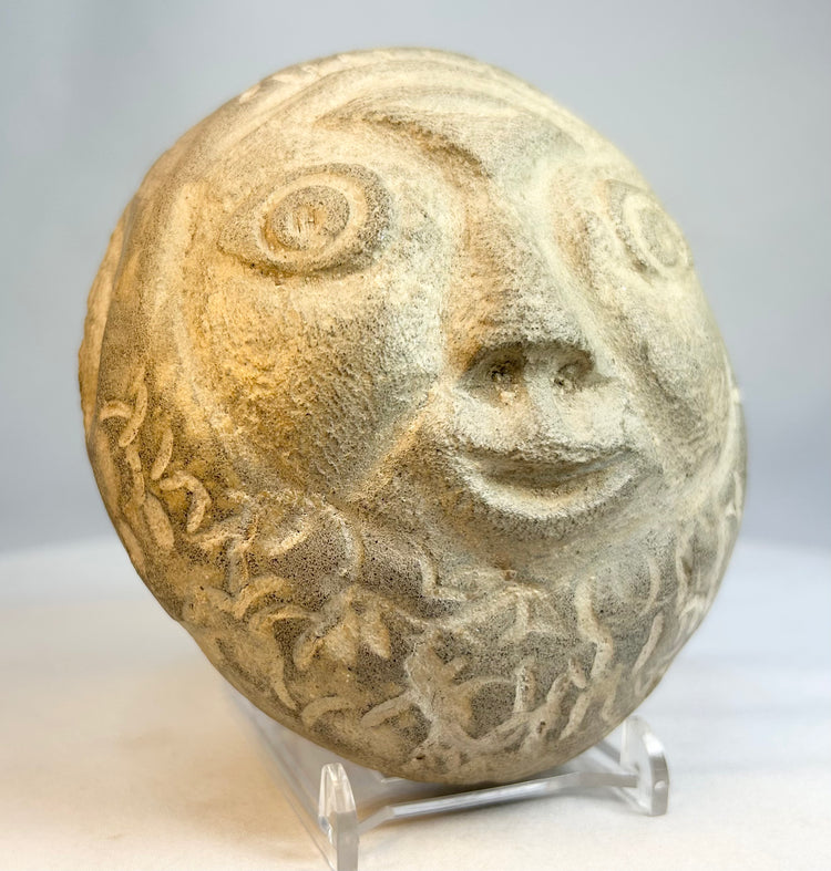 Vintage carved stone face sculpture photographed against neutral background