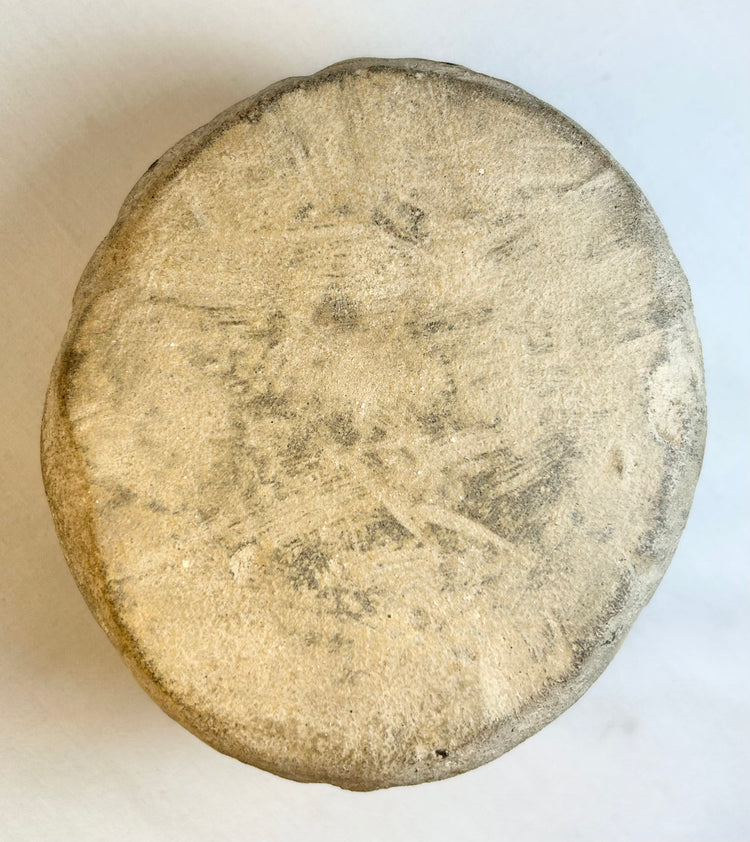 Back view of rounded stone face sculpture displayed on clear stand with natural patina