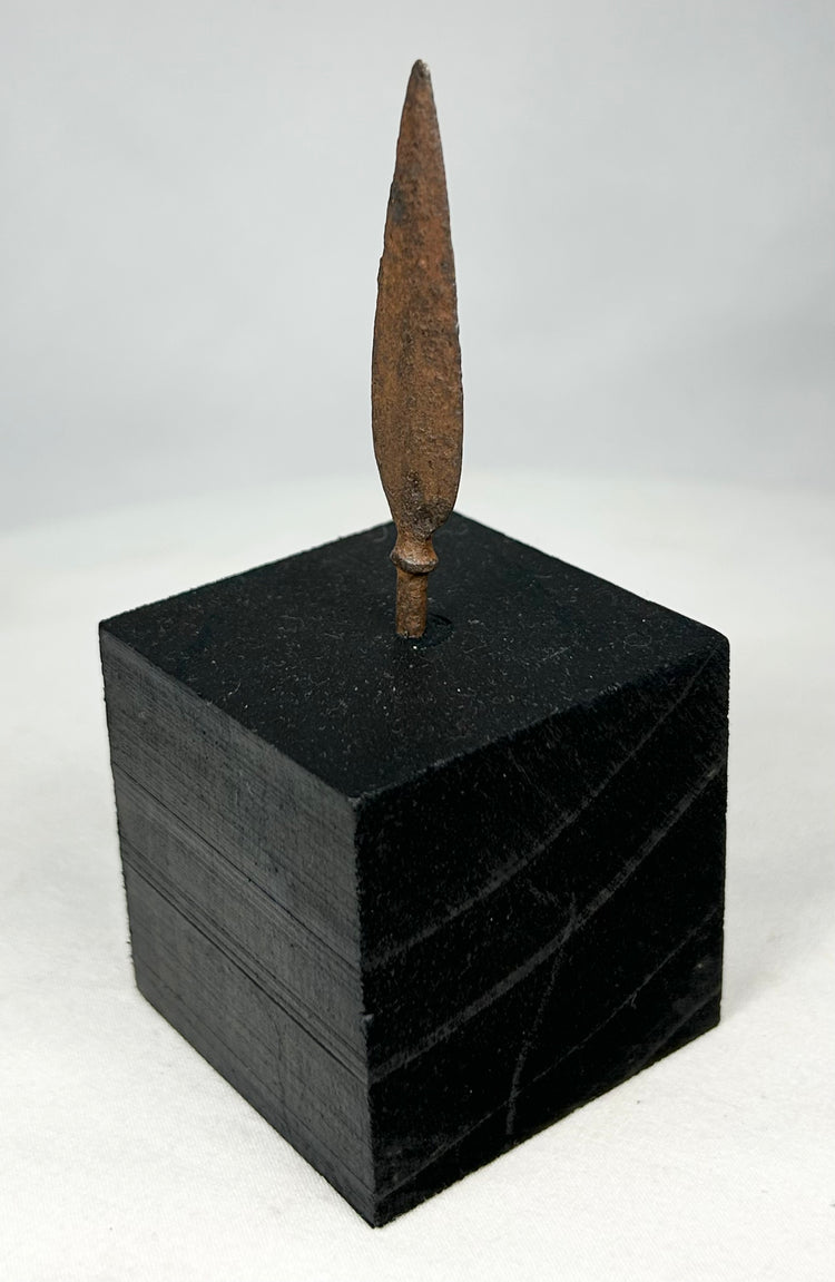 Side profile of leaf-blade iron arrowhead mounted on museum-style black stand