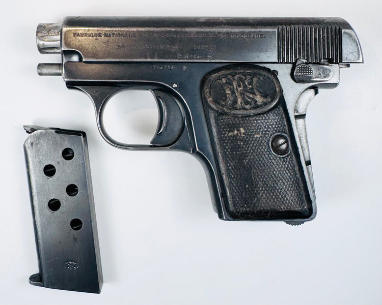 Deactivated FN Browning Model 1906 with its slide held open and a detached steel magazine displayed beside it.
