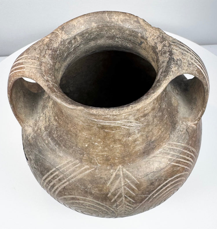 Rear-side angle of the Etruscan vessel showing both handle attachments and a large incised spiral decorating the rounded body.