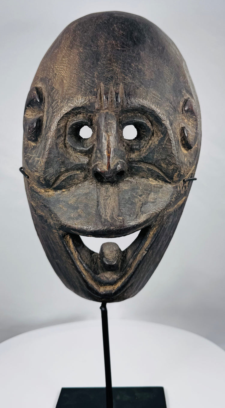 Indonesian ritual mask from West Timor with pierced eyes, open mouth, and weathered carved wood surface.