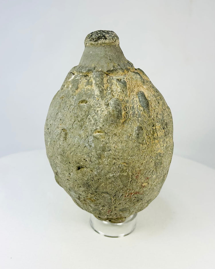 Angled view of an Islamic ceramic hand grenade from Greater Persia, 10th–12th century CE, displaying its textured surface, globular body, and aged patina on a white background.