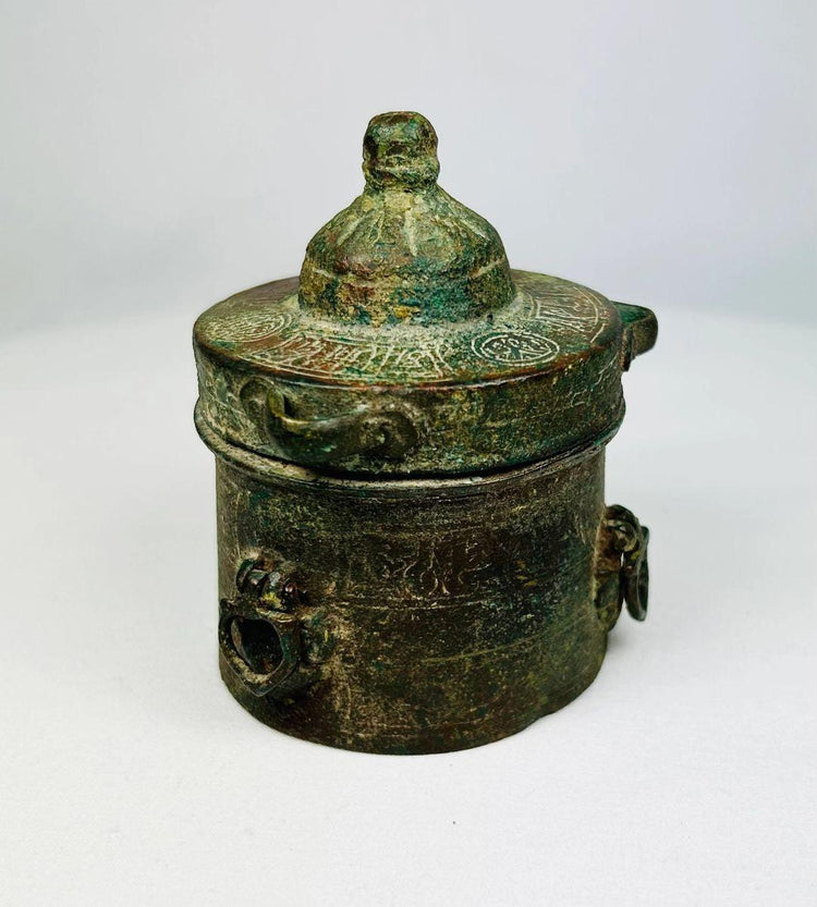 Antique Islamic Khorassan bronze inkwell, cylindrical form with domed lid, engraved with intricate geometric and vegetal motifs, rich green patina from centuries of age, dating to the 10th–12th century, historically used by Islamic scholars and scribes as part of manuscript tradition.