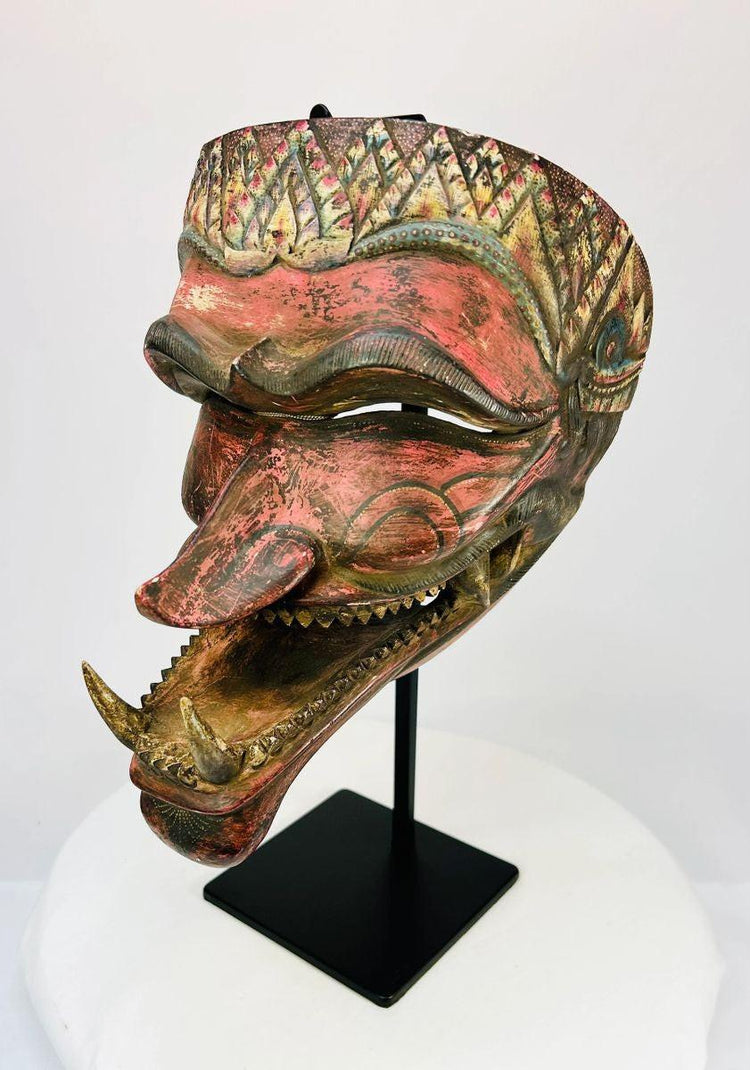 Late 19th-century Javanese carved wooden Cakil mask with polychrome paint displayed on a black stand.
