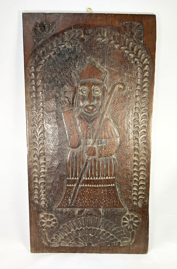 Hand-carved hardwood devotional panel depicting a bishop saint, likely St. Nicholas, with crozier and blessing gesture, foliate border with rosettes, Central/Eastern Europe, c. 1780–1830, 18 7/8 x 9 3/4 inches