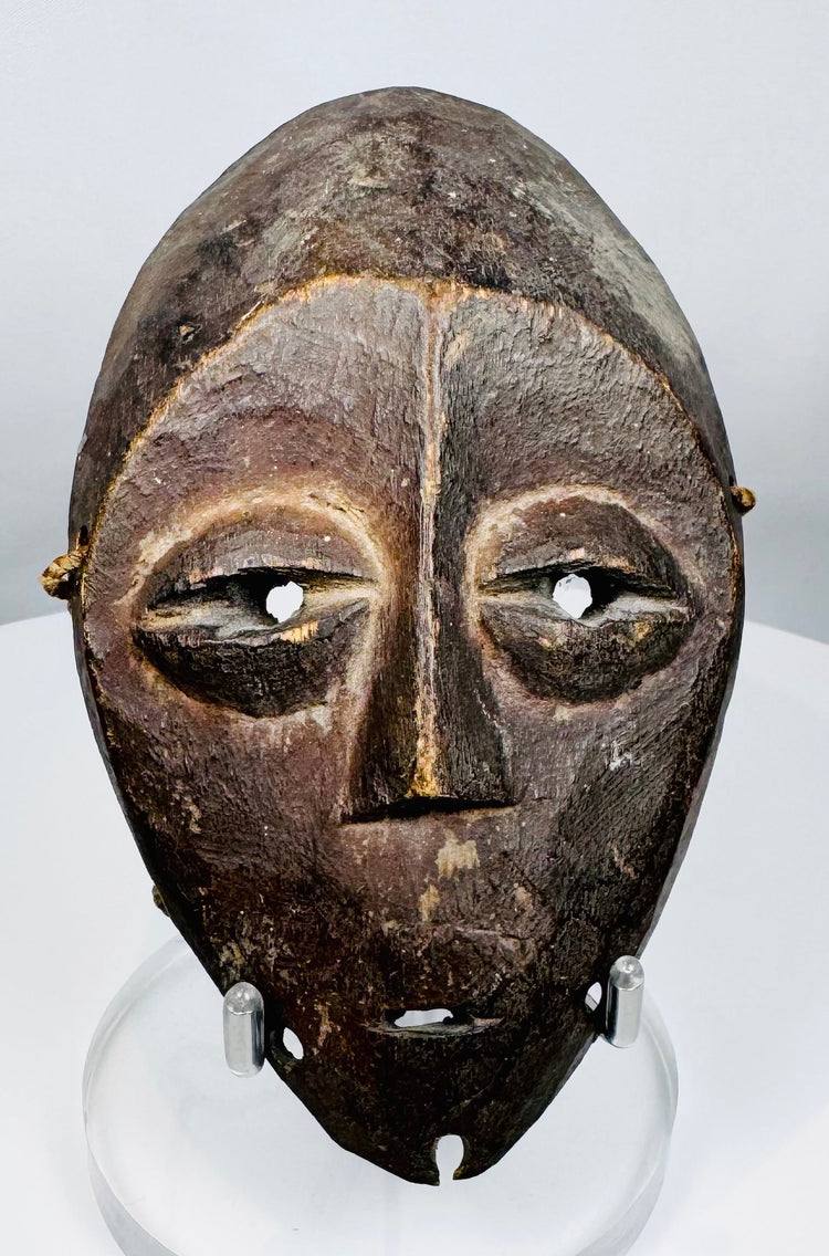 Central African Lega mask featuring simplified symbolic facial features and original fiber cord remnants.