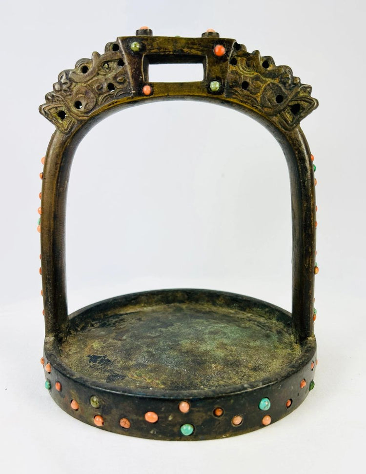 Ornate cast bronze stirrup from Mongolia or Himalayan region, featuring dragon-head terminals, pierced latticework, and hand-set coral, turquoise, and glass inlays, 7 inches tall by 6 inches wide, with natural patina and verdigris, circa 18th century.