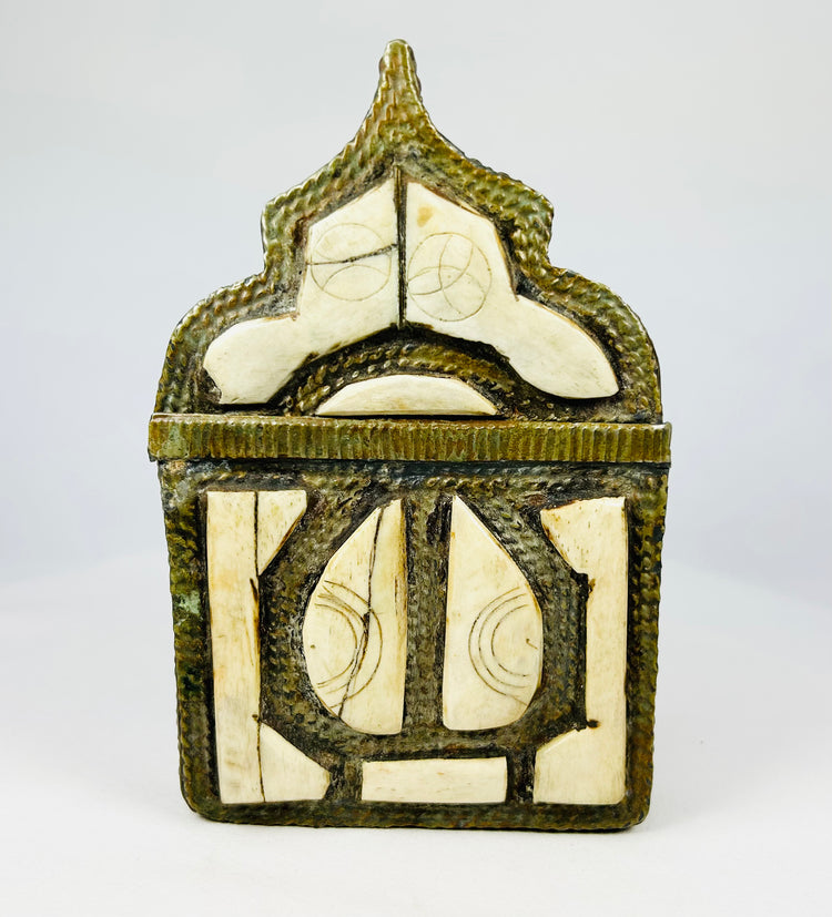 Ornate 19th-century Moroccan Berber amulet box with hinged pointed-arch lid, hammered brass body, carved bone inlay with geometric designs, and rich patina, used to house protective talismans and Quranic verses
