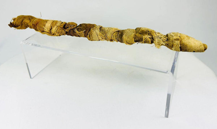 Mummified juvenile crocodile from Ancient Egypt, Late Period to Early Roman era, wrapped in linen as a votive offering to the god Sobek, displayed on a clear stand.