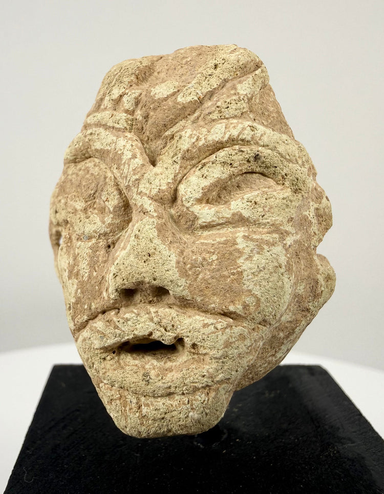 Carved limestone head fragment inspired by ancient Near Eastern votive traditions, mounted on a modern black display stand.