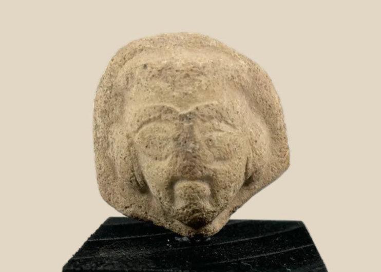 Fragmentary terracotta head with stylized arched brows, almond-shaped eyes, defined beard and mustache, and detailed coiffure; likely part of a votive or ritual figure from the Near East/Eastern Mediterranean, circa 1st millennium BCE; mounted on a custom black display base.