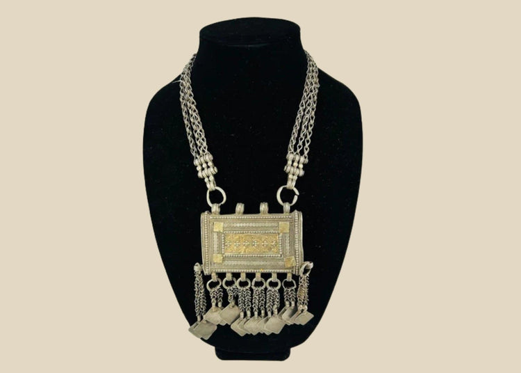 19th-century Omani silver hirz necklace with central rectangular Koran holder, intricate filigree and gilded accents, suspended from a multi-strand chain with decorative dangles.