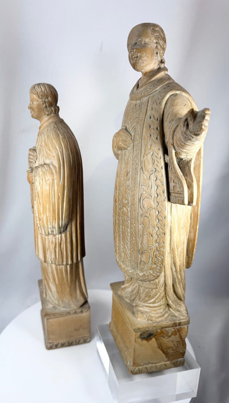 Antique wooden religious statues featuring a bearded cleric and youthful saint holding a symbolic attribute.