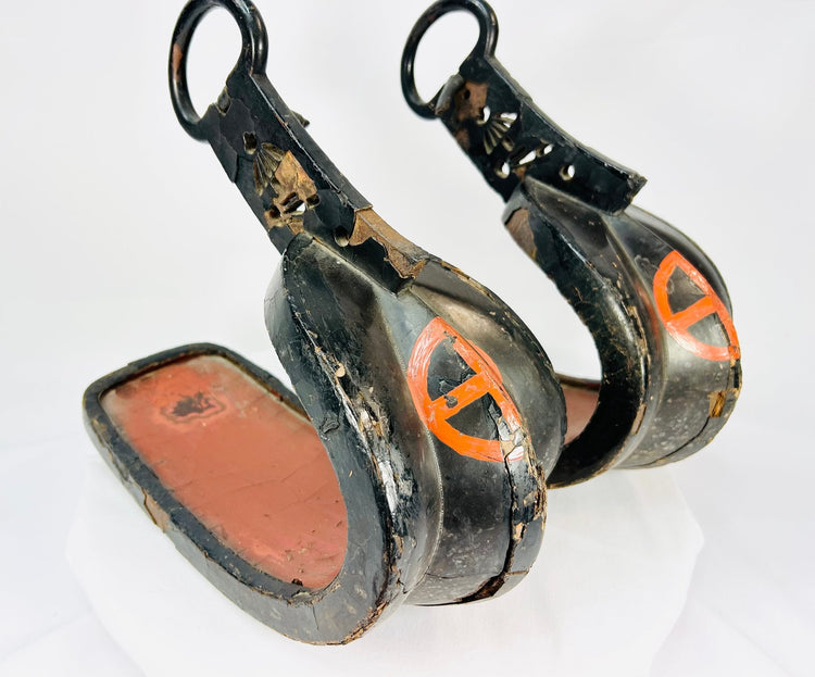 Pair of antique Japanese lacquered samurai stirrups from the Edo–Meiji period, black lacquer with red cross-in-circle mon crest, displayed on a white background – Relic & Rarity.