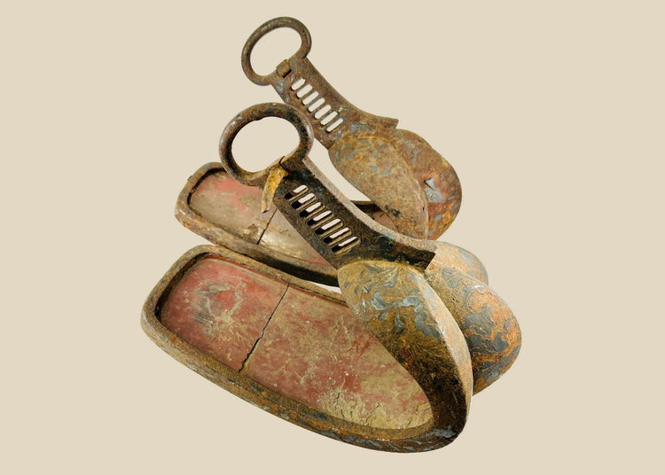 Matched pair of late 18th–mid-19th-century Japanese abumi stirrups with hand-forged iron, broad scooped treads, triple-lobed toe guards, red interior lacquer, black/brown exterior lacquer remnants with painted scrollwork, large suspension rings, Edo period, circa 1770–1860.