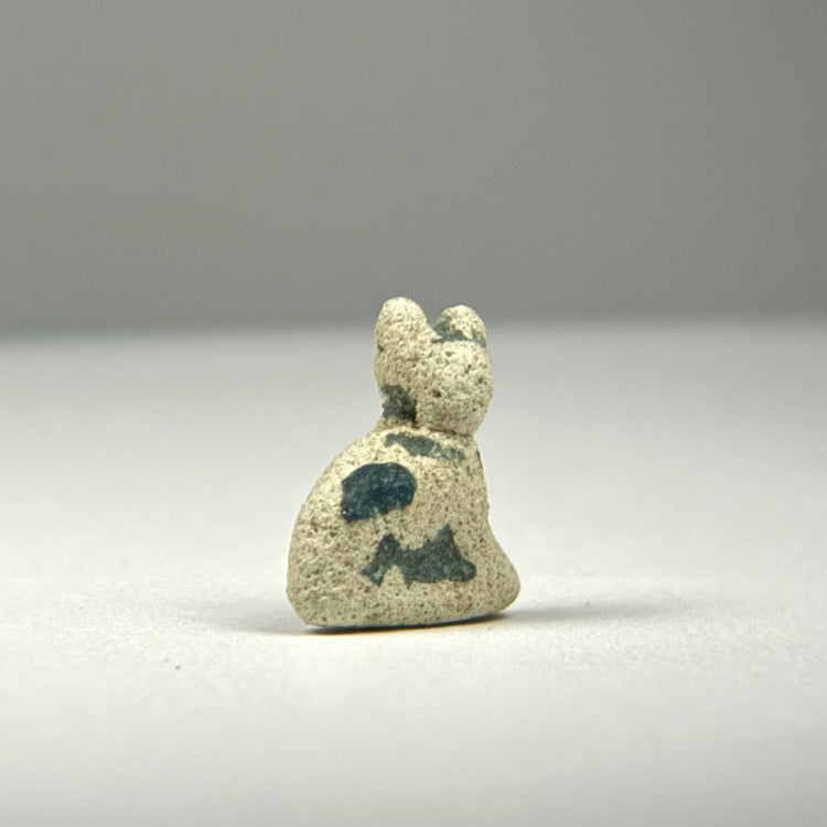 Close detail of an Ancient Egyptian Bastet cat amulet with modeled feline features, mineral deposits, and worn ancient glaze.