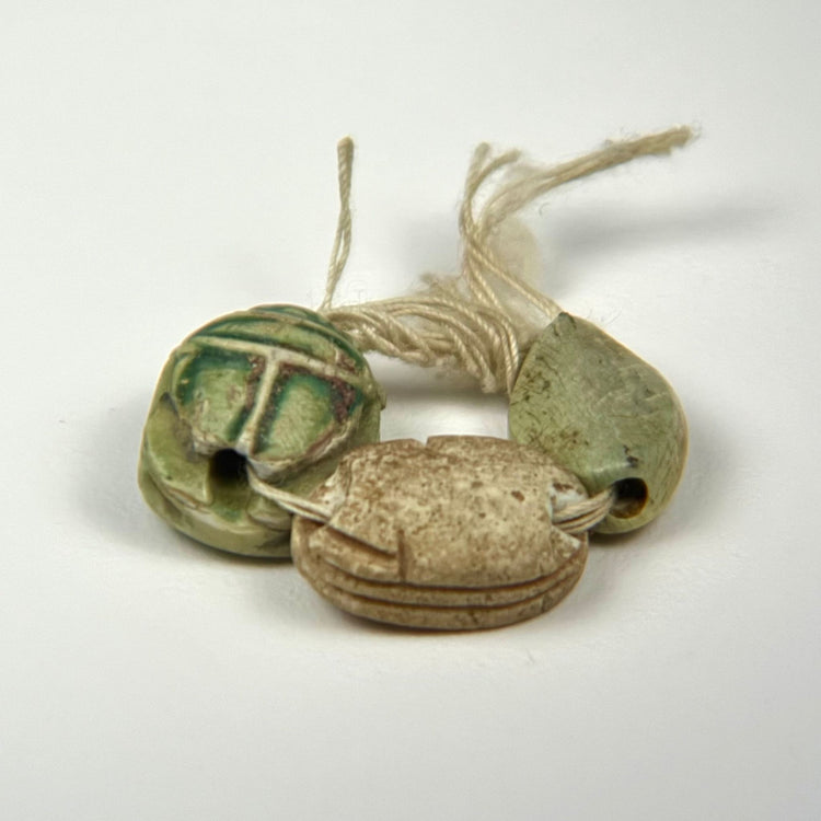 Three Ancient Egyptian scarab charms with varied surface preservation, carved details, hieroglyphic markings, and traces of green glaze.