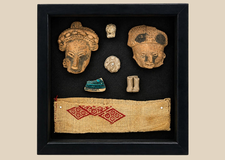 Flat-lay view of Pre-Columbian artifact collection in black shadowbox featuring clay masks and carved stone