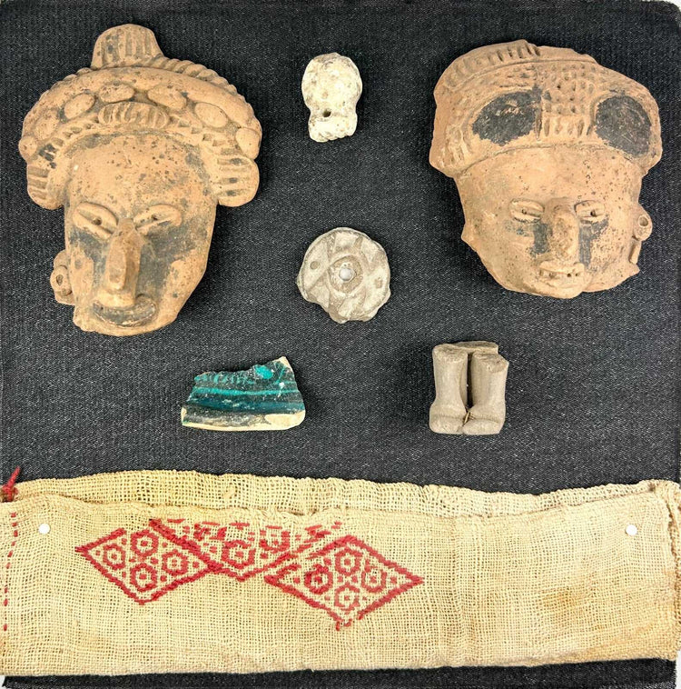 Pre-Columbian shadowbox with terracotta fragments, figurines, and red patterned textile on white background