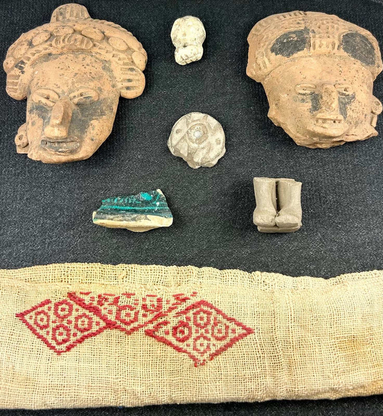 Pre-Columbian artifacts in black shadowbox, including figurines, mask shards, and geometric textile
