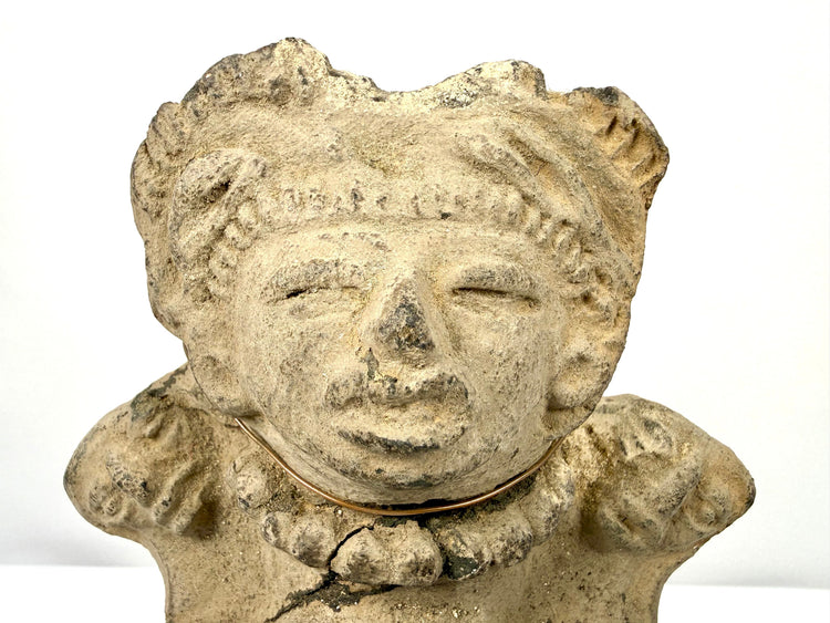 Detail of upper figure's closed slit eyes and elaborate headdress on light brown clay