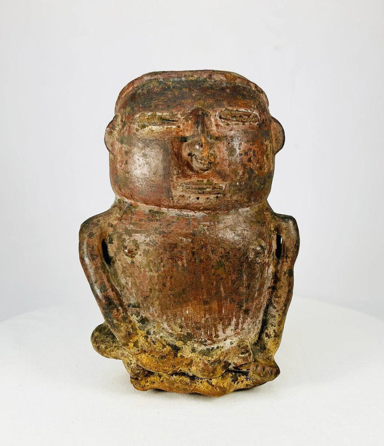 A Pre-Columbian terracotta effigy vessel depicting a seated human figure with stylized facial features, hands on lap, and an opening at the top of the head for offerings, dating to circa 500 BCE–900 CE.
