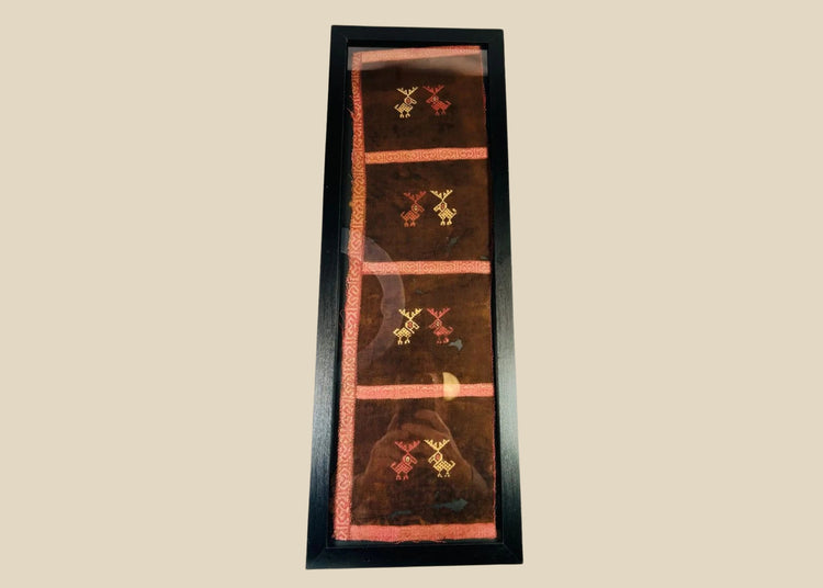 Ancient Pre-Columbian textile fragment featuring geometric animal motifs embroidered in red, gold, and tan thread on a dark brown woven ground, preserved in a protective display frame, dating to circa 1000–1400 CE, representing Andean artistry and symbolic ritual use.