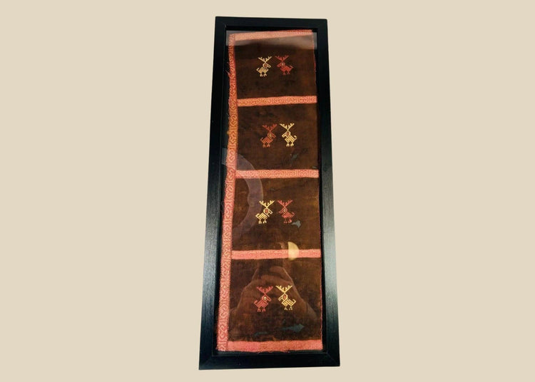 Ancient Pre-Columbian textile fragment featuring geometric animal motifs embroidered in red, gold, and tan thread on a dark brown woven ground, preserved in a protective display frame, dating to circa 1000–1400 CE, representing Andean artistry and symbolic ritual use.