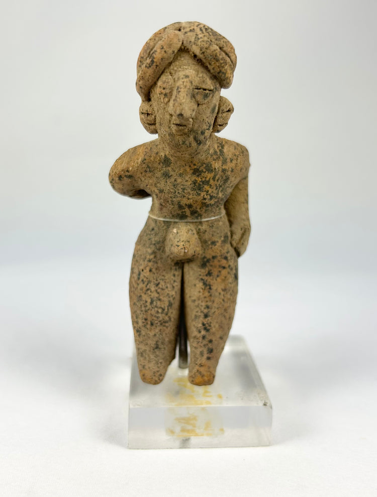 Pre-Columbian West Mexican terracotta standing figure, circa 300 BCE–500 CE, hand-modeled with tall turban-style headdress, stylized proportions, and surface encrustations, mounted on acrylic display base