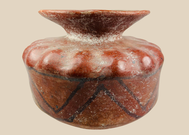 Pre-Columbian globular ceramic vessel with scalloped body and red-orange geometric painted designs on a white background.