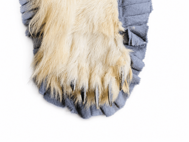 Close-up detail of a polar bear rug paw showing the natural fur, long claws, and grey ruffled fabric edging.