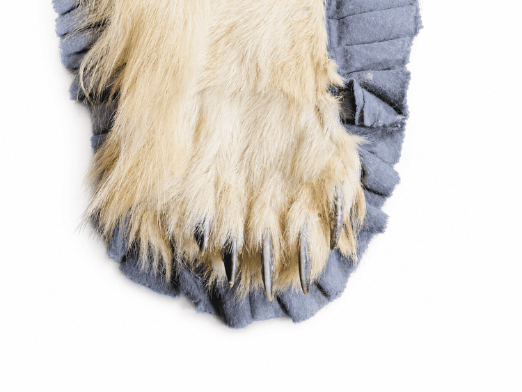Close-up detail of a polar bear rug paw showing the natural fur, long claws, and grey ruffled fabric edging.